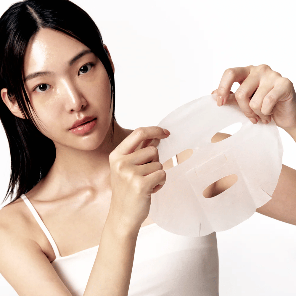 Vrouw met schone en gehydrateerde huid houdt een witte Sheet mask voor zich, klaar om deze op het gezicht aan te brengen.