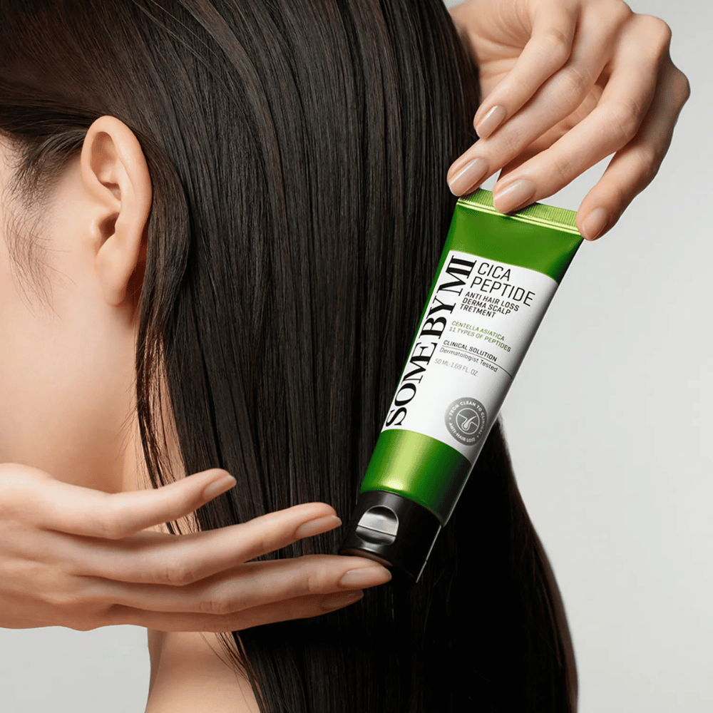 Vrouw brengt SOME BY MI Cica Peptide Anti Hair Loss Derma Scalp Treatment aan in lang, donker haar met een groene en witte tube.
