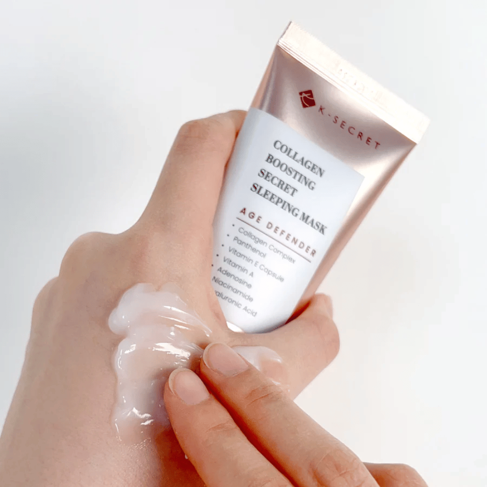 Een hand houdt Collagen Boosting Secret Sleeping Mask vast terwijl de andere een royale hoeveelheid crème op de bovenkant van de hand aanbrengt - toont de textuur en toepassing van het product.
