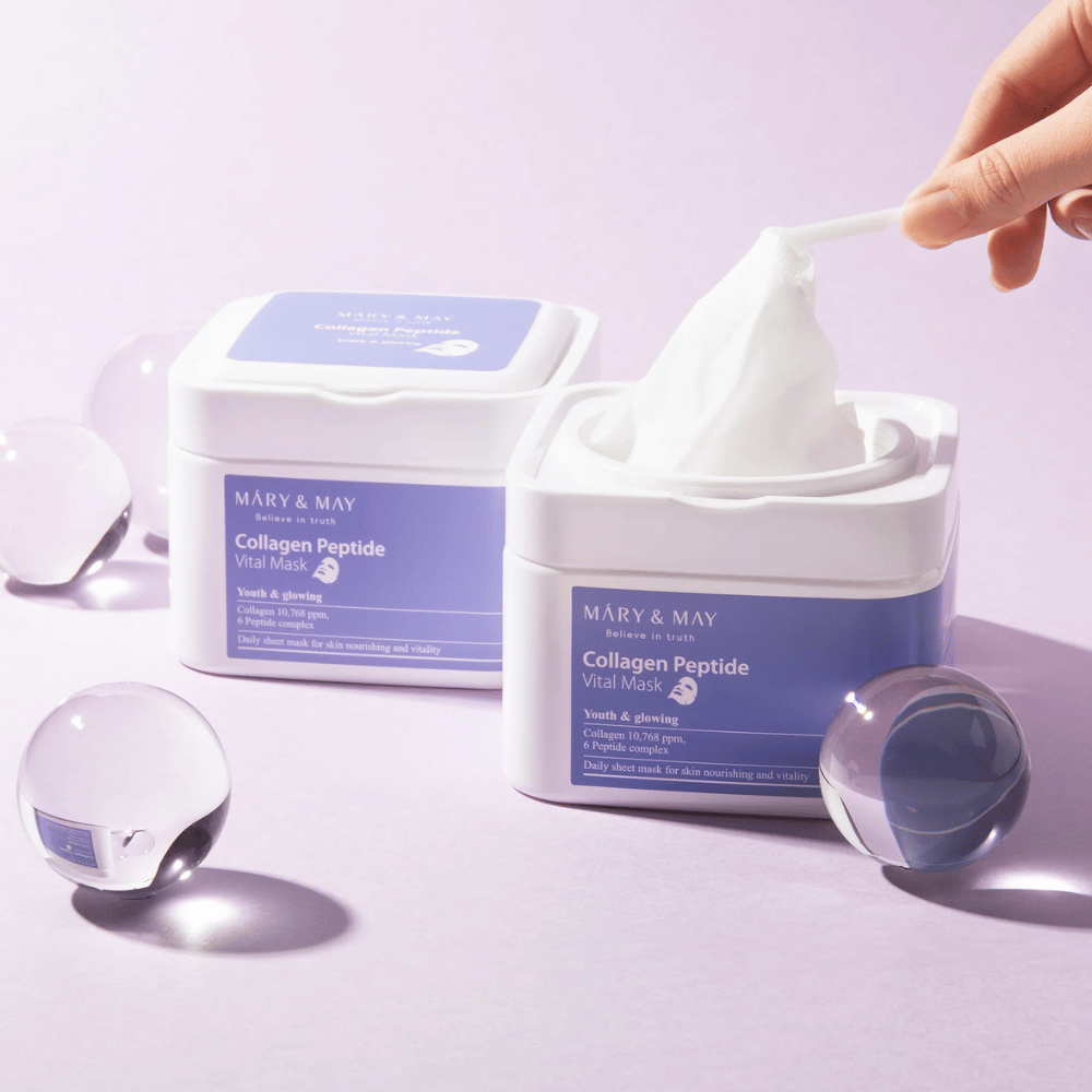 Een hand neemt een masker uit een pot van MARY & MAY Collagen Peptide Vital Mask. Het masker is bedoeld voor dagelijks gebruik om de huid te voeden en te laten stralen, met collageen en peptiden om de jeugdigheid van de huid te ondersteunen.