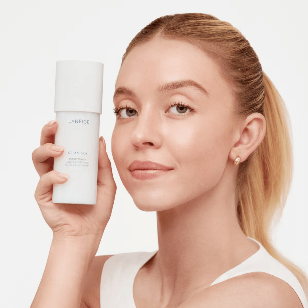 Een persoon houdt Laneige Cream Skin Cerapeptide Refiner in een witte fles omhoog. De persoon glimlacht en toont het product, dat wordt gepromoot als een hydraterende toner en huidverzorgingsproduct.