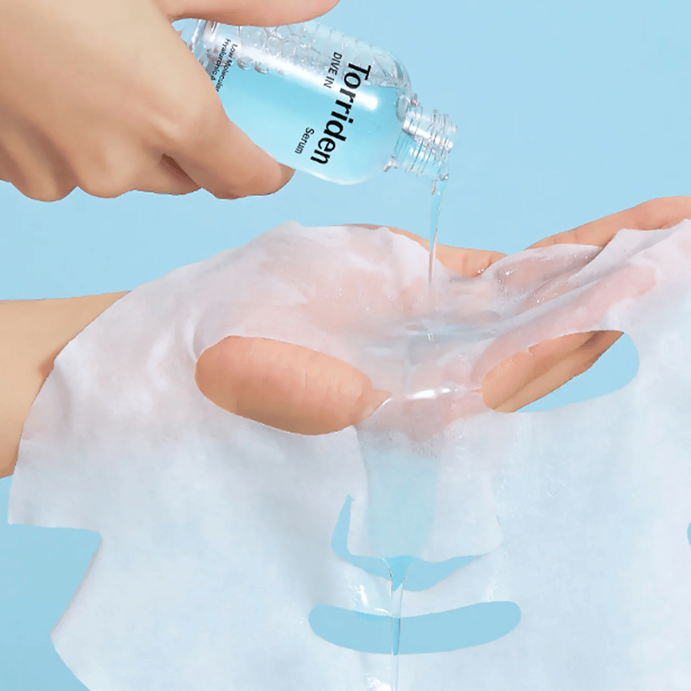 Gezichtsmasker dr bedekt met oplossing uit een fles "Torriden Dive-In", tegen een blauwe achtergrond.