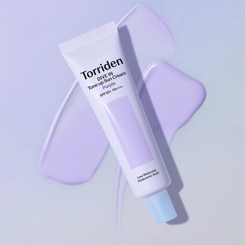 Torriden DIVE IN Tone Up Sun Cream Purple geplaatst op uitgesmeerde paarse crème die het egaliserende en glansgevende effect benadrukt.