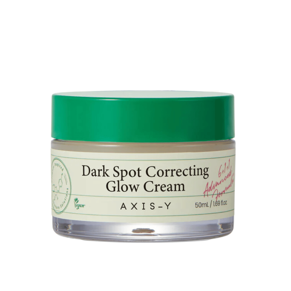 Een pot van "AXIS-Y Dark Spot Correcting Glow Cream". Deze crème is bedoeld om donkere vlekken te corrigeren en de huid te laten stralen. De verpakking is elegant met een transparante bodem en een opvallend groen deksel.