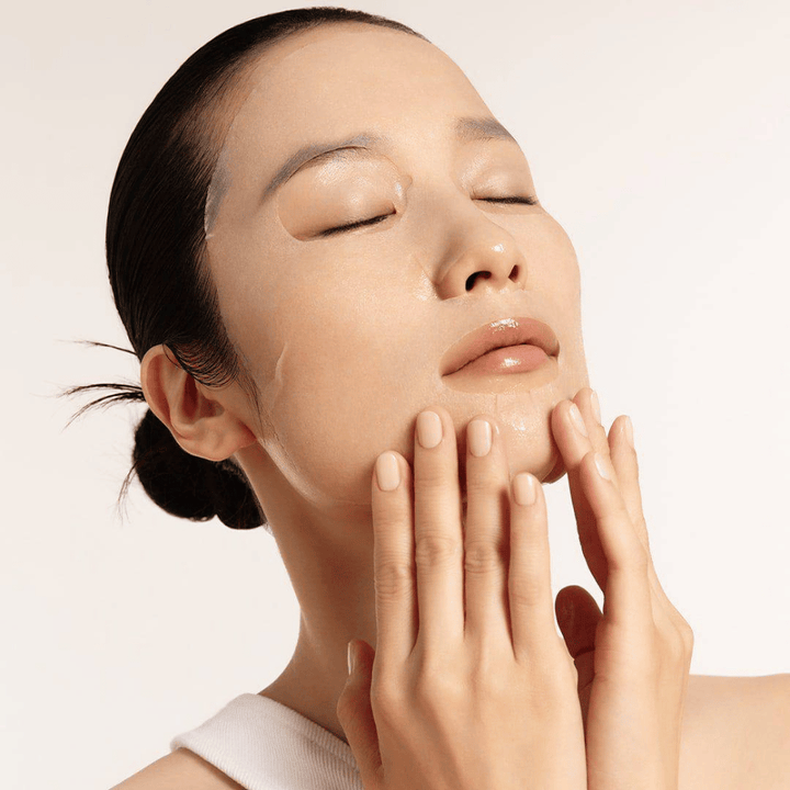 Model met gehydrateerde en stralende huid brengt Sheet mask aan, focus op glans, egale teint en glow.