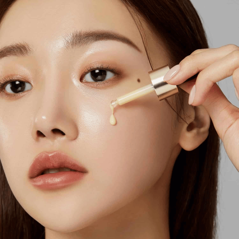 Close-up van een vrouw die Medicube Deep Vita C Ampoule aanbrengt met een goudkleurige pipet. Een druppel van het serum is op weg naar haar huid, die een natuurlijke glans heeft. Perfect om een helderdere en egalere huidtint te geven.