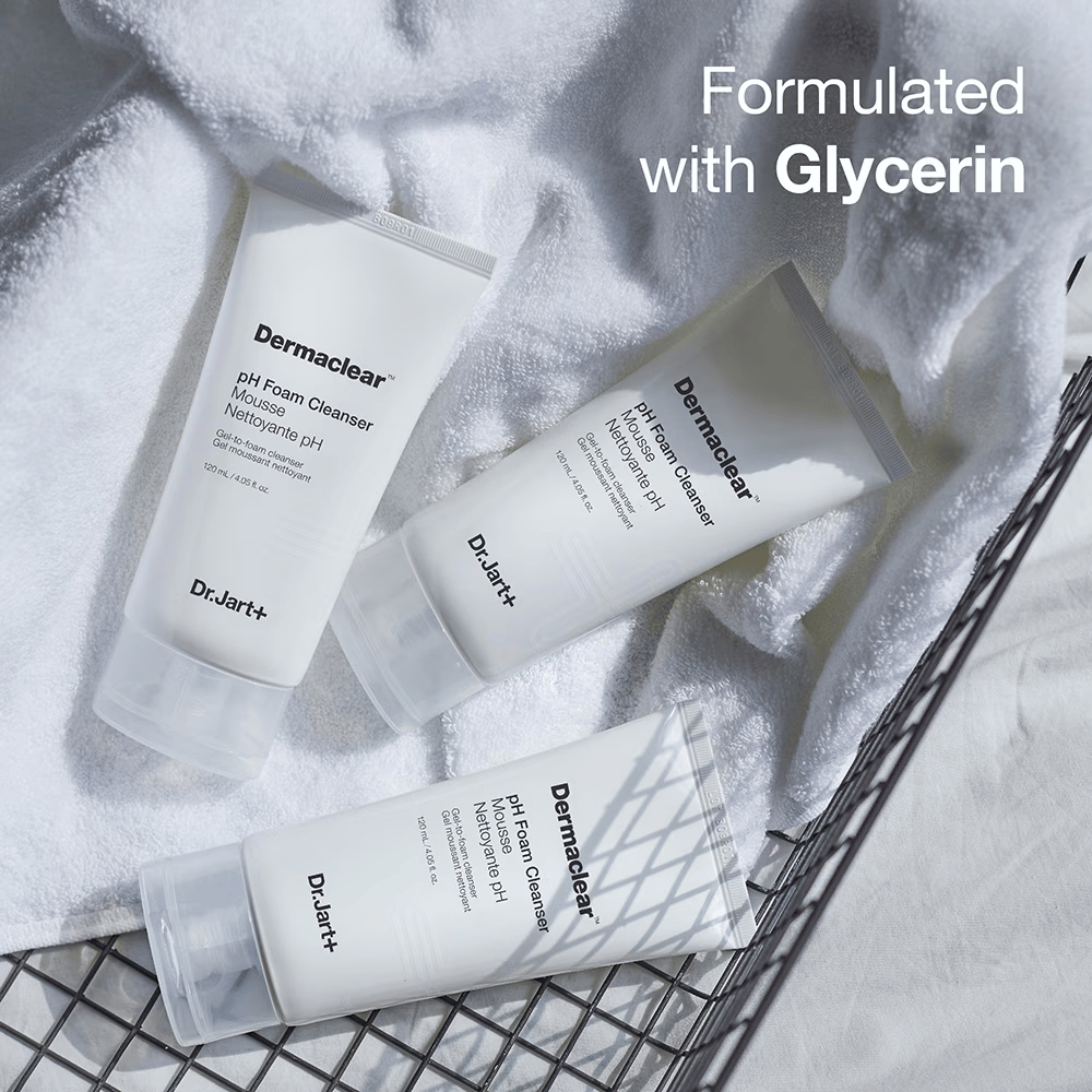Drie tubes van Dr.Jart+ Dermaclear pH Foam Cleanser liggen op een witte badstof handdoek in een metalen mand, met de tekst "Formulated with Glycerin" in de bovenhoek.