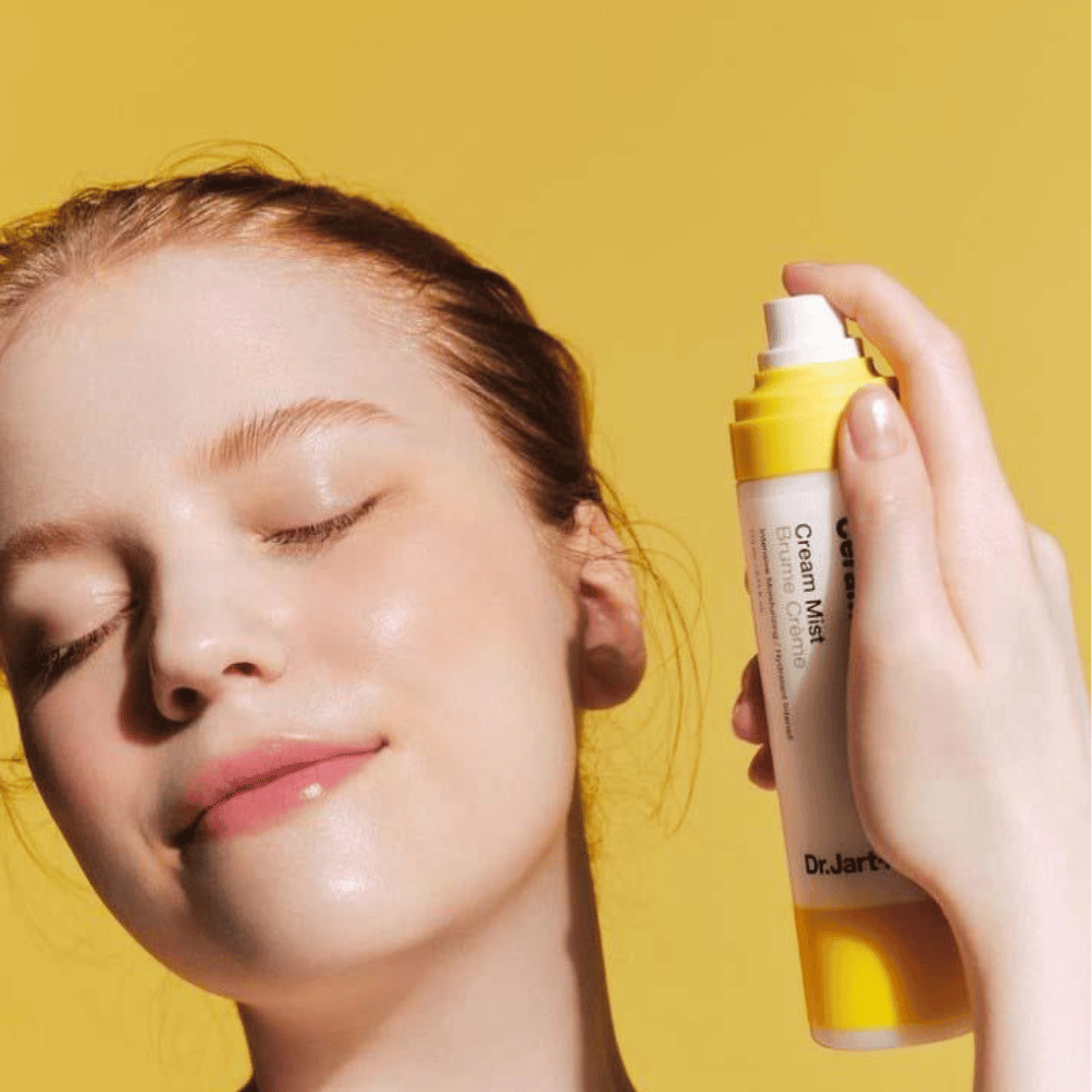Een vrouw houdt een fles Dr. Jart+ Ceramidin Cream Mist 110ml bij haar gezicht, wat de vocht-boost voordelen en veganistische formulering promoot.
