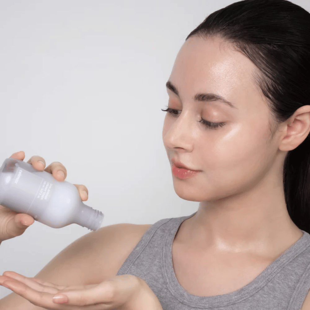 Vrouw met glanzende, gehydrateerde huid brengt Celimax Dual Barrier Creamy Toner aan door het product in haar handpalm te gieten voor haar huidverzorgingsroutine.