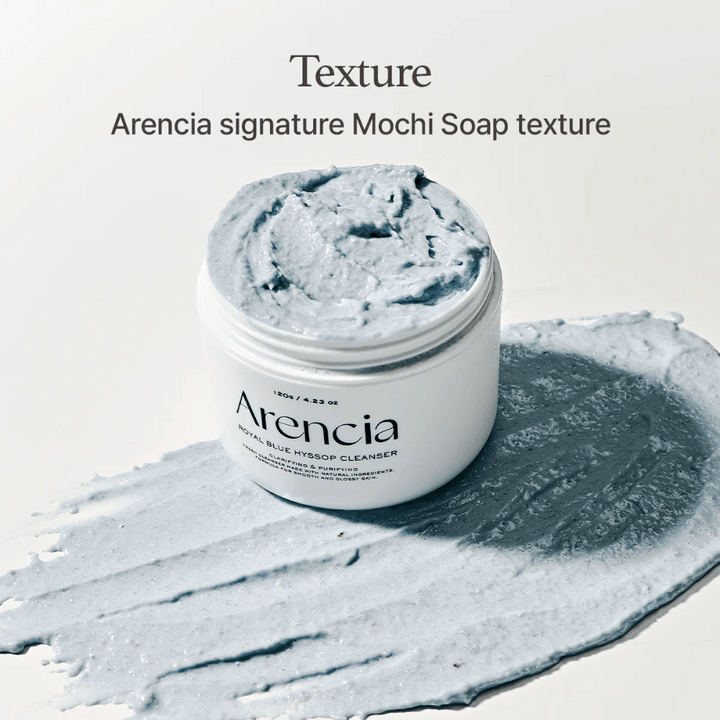 Öppen burk med Arencia Fresh Blue Hyssop Rice Mochi Cleanser, placerad ovanpå ett utsmetat lager av den blå, krämiga rengöringsformulan som visar dess mochi-liknande textur.
