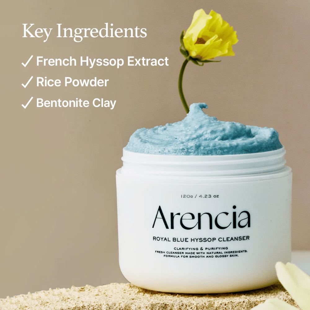 Afbeelding van de pot "Arencia Royal Blue Hyssop Cleanser" gevuld met blauwe reinigingscrème. Een gele bloem steekt uit de crème. De tekst in de afbeelding benadrukt drie sleutelingrediënten: Franse Hyssop-extract, rijstpoeder en bentonietklei.