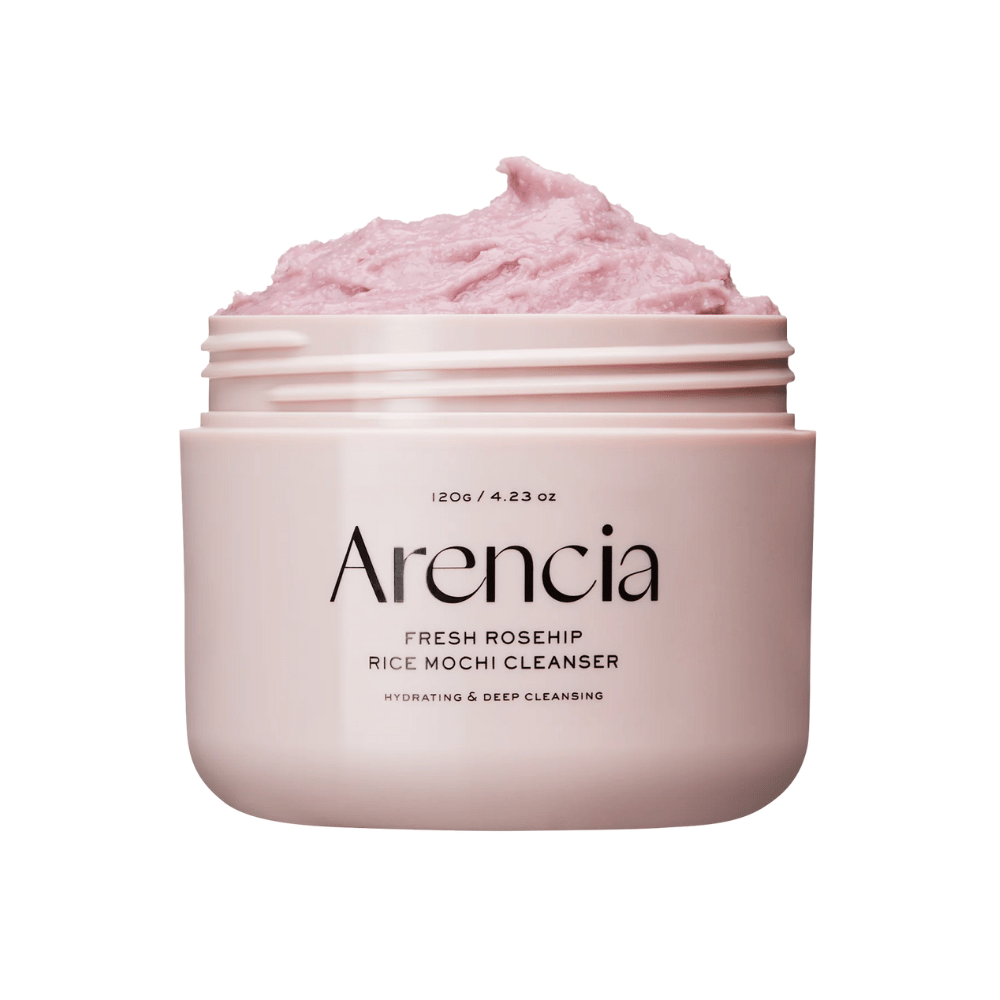 Close-up van een roze pot met Arencia Royal Rosehip Cleanser, gevuld met roze reinigingscrème met een opgeklopte, mochi-achtige textuur. De tekst op de pot geeft aan dat het product hydrateert en diep reinigt.