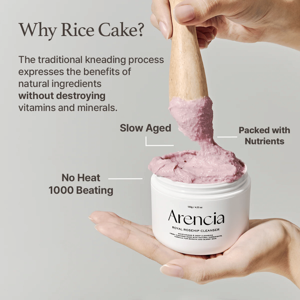 Een hand houdt een open pot van Arencia Royal Rosehip Cleanser vast, met een roze, mochi-achtige reinigingsformule die met een houten spatel wordt opgetild - toont de textuur en traditionele productiemethode van het product.