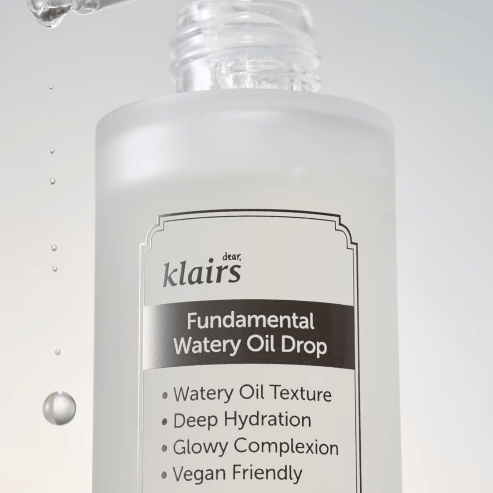 Close-up van de fles Klairs Fundamental Watery Oil Drop, met tekst die de eigenschappen van het product benadrukt zoals "Watery Oil Texture", "Deep Hydration", "Glowy Complexion" en "Vegan Friendly".
