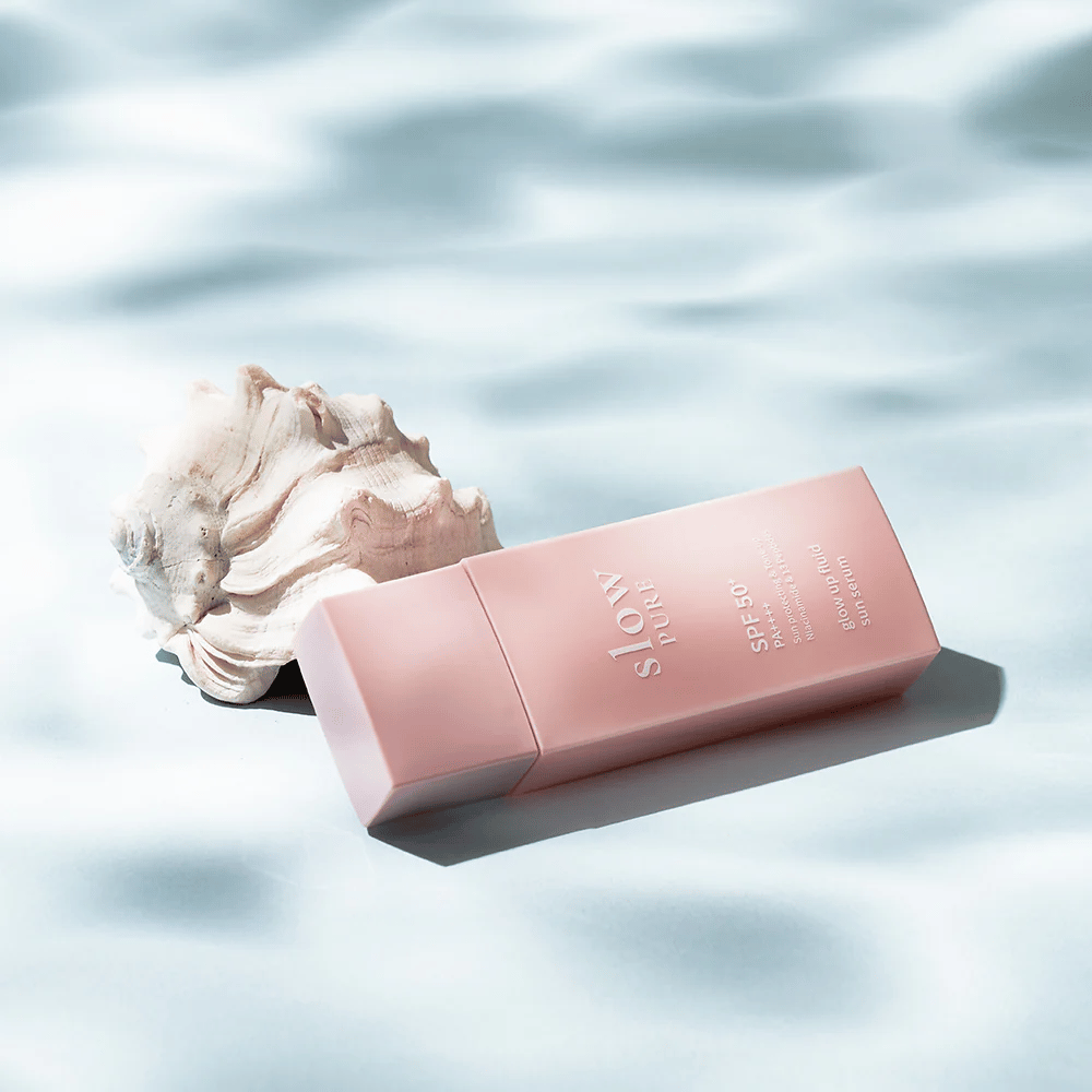 Slow Pure Glow Up Fluid Sun Serum bij schelp en watereffect, benadrukt zonbescherming en glans.