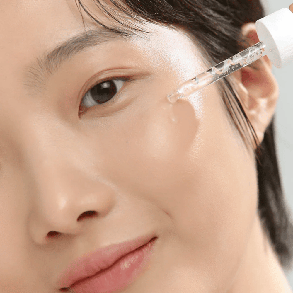 Close-up van een vrouw die serum op de wang aanbrengt met een pipet - huidverzorging die glans en hydratatie geeft.