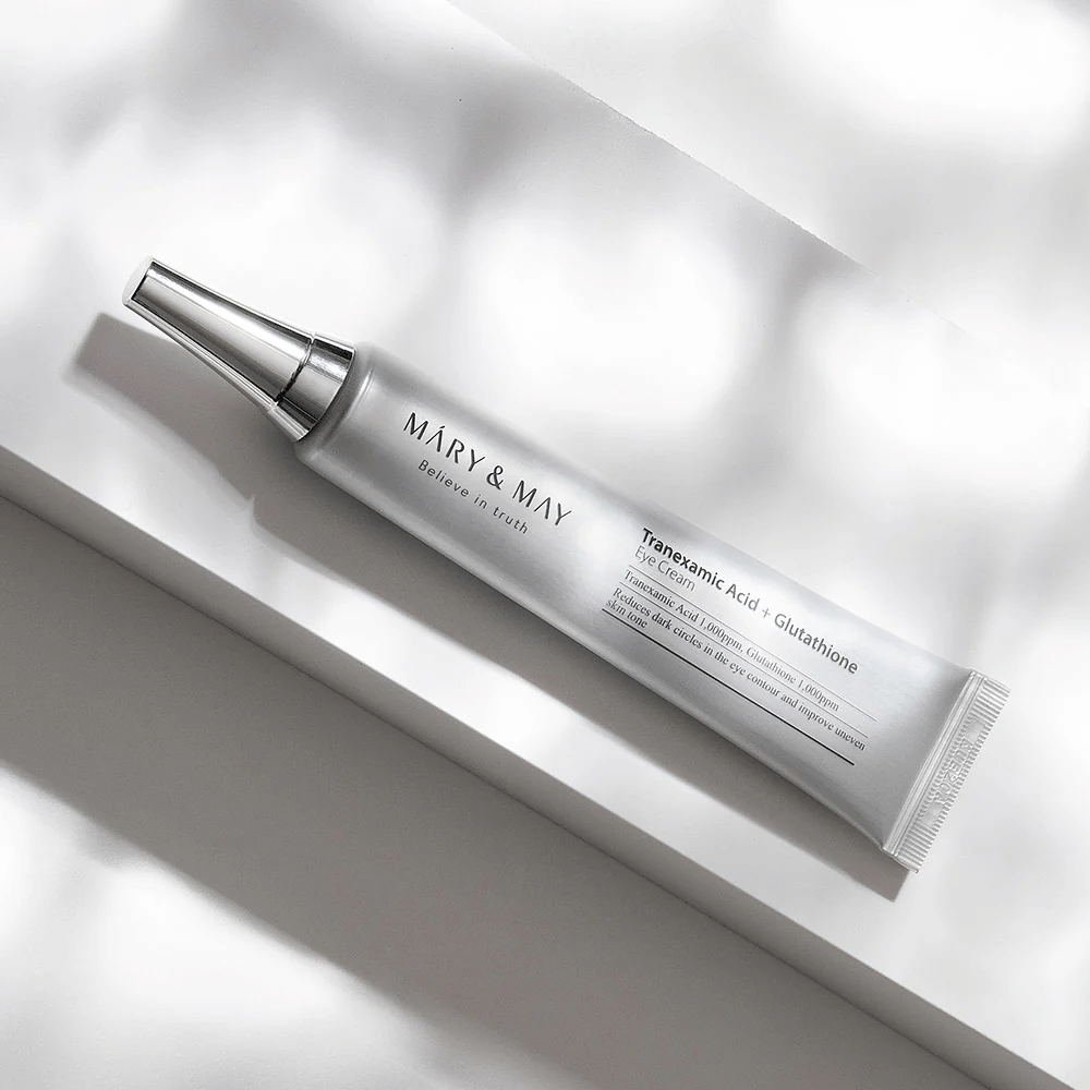 Close-up van Mary&May Tranexamic Acid + Glutathione Eye Cream met metalen applicator, ontwikkeld om donkere kringen op te lichten en de huidtint rondom de ogen te egaliseren.