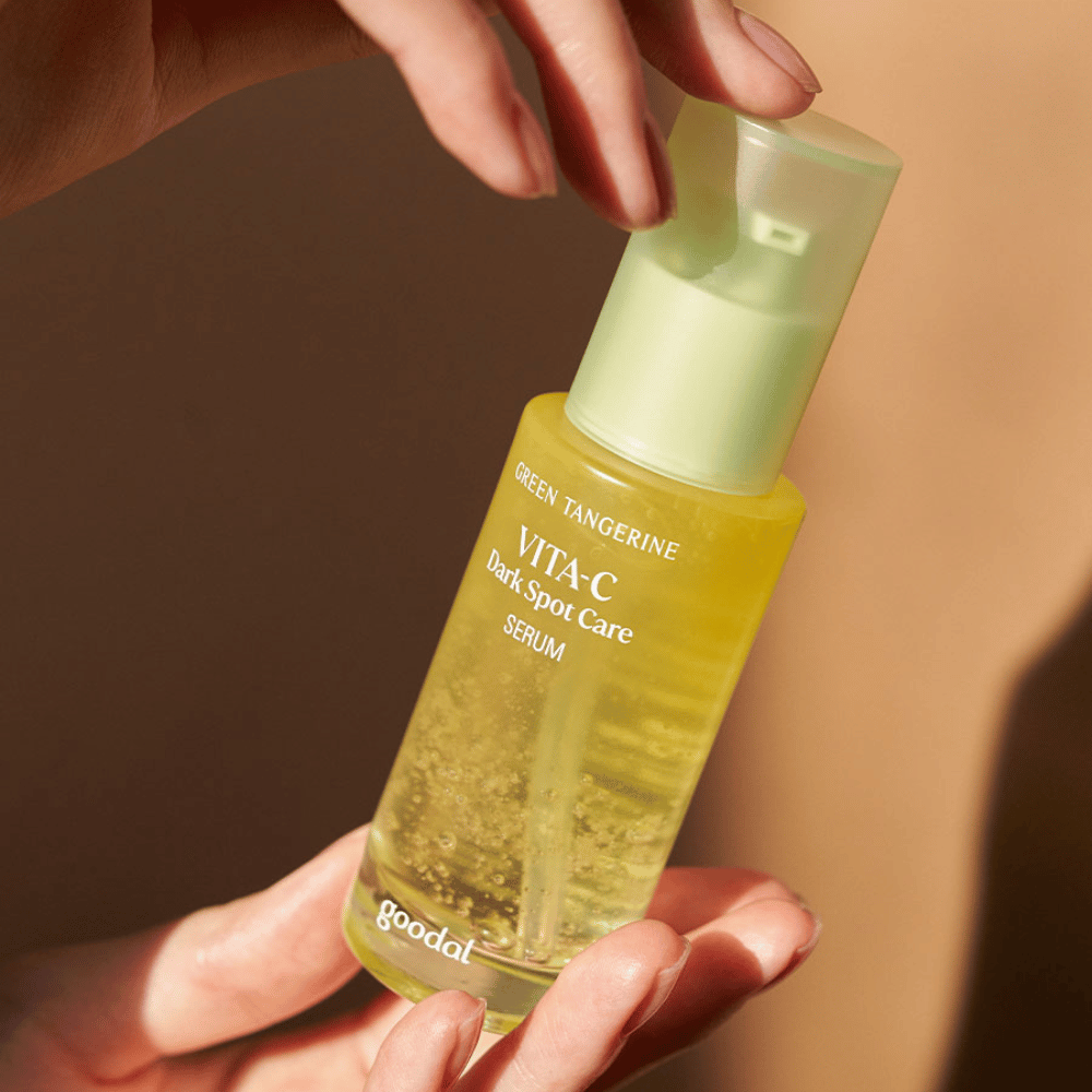 Een persoon die een fles Green Tangerine Vita C Dark Spot Care Serum 40ml van Goodal houdt voor hyperpigmentatie en verzorging van donkere vlekken.