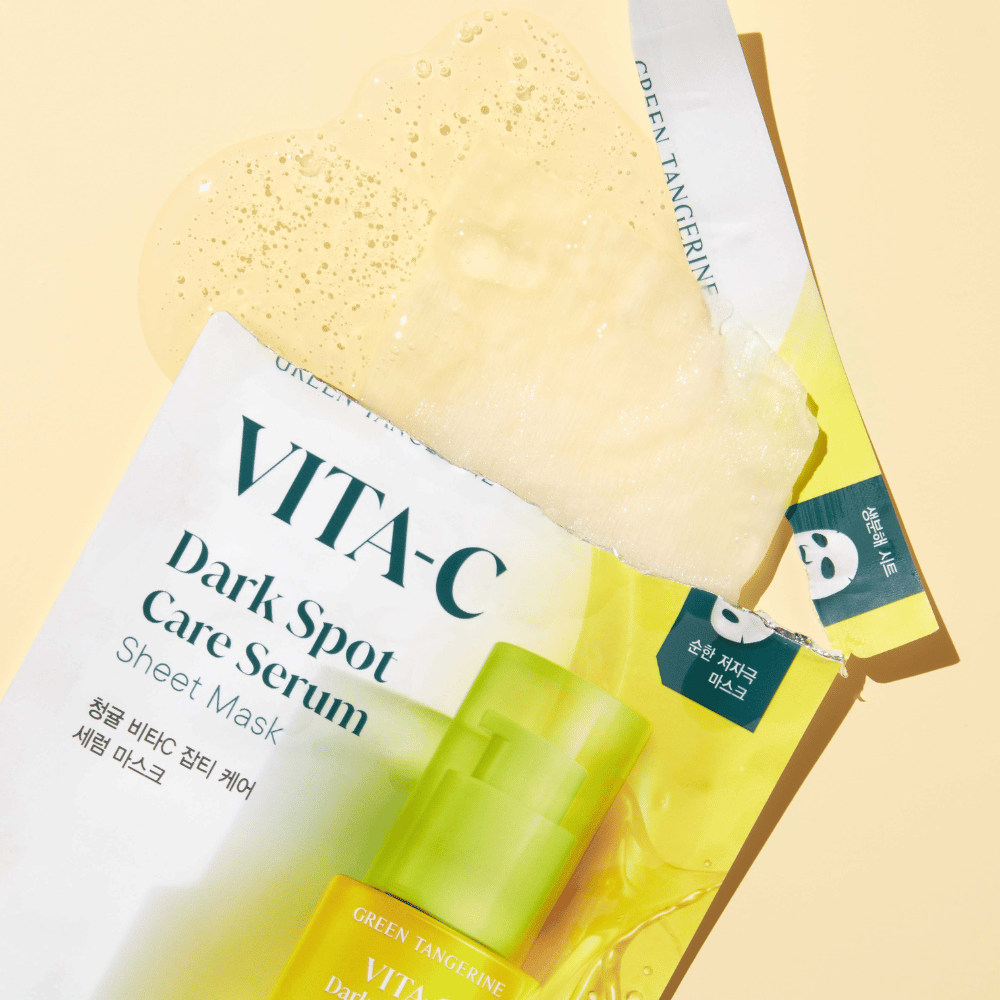 Geopende verpakking van VITA-C Dark Spot Care Serum Sheet mask met een gezichtsmasker erop en een groene serumfles, allemaal tegen een gele achtergrond.