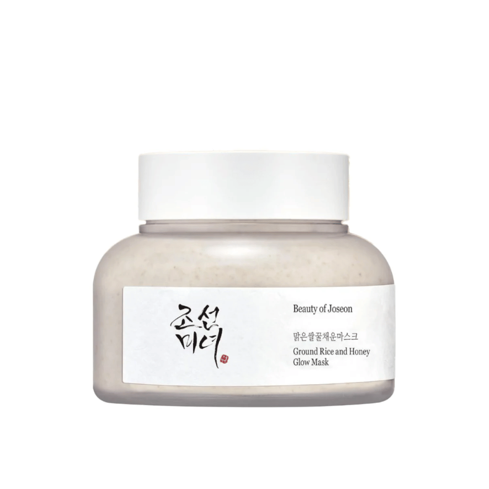 Een pot "Beauty of Joseon Ground Rice and Honey Glow Mask". De verpakking is eenvoudig met een witte dop en een etiket dat de productnaam en ingrediënten in zowel het Koreaans als Engels presenteert. Het product is ontworpen om de huid te laten stralen en te voeden.