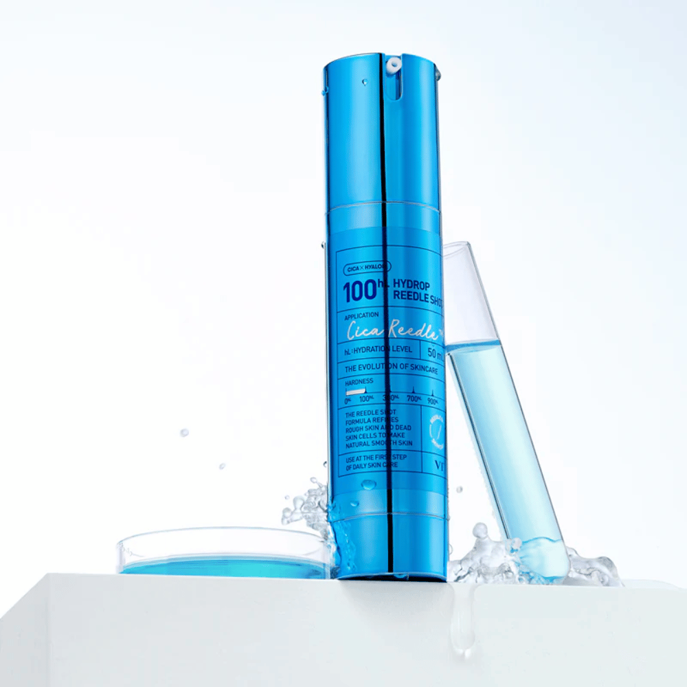 Blauwe fles VT Cica Hyalon Hydrop Reedle Shot 100hL staande op een wit oppervlak met waterspetters, naast een reageerbuis gevuld met blauwe vloeistof en een rond deksel met dezelfde vloeistof.
