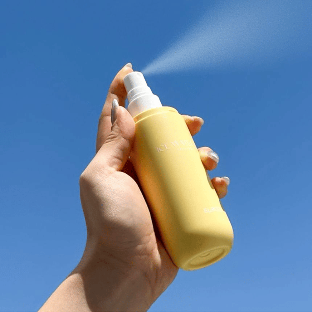 ELROEL Ice Water Sun Mist SPF 40 PA+++ zonnemistspray wordt uit een fles tegen een blauwe hemel gesprayd, lichte zonnebescherming die de huid hydrateert en verfrist