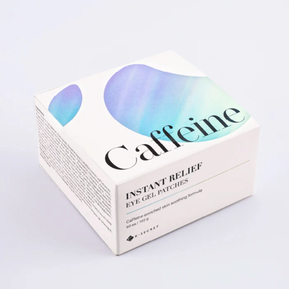 Verpakking van K-Secret Instant Relief Eye Gel Patches met cafeïne in wit ontwerp met blauwe en groene tinten.