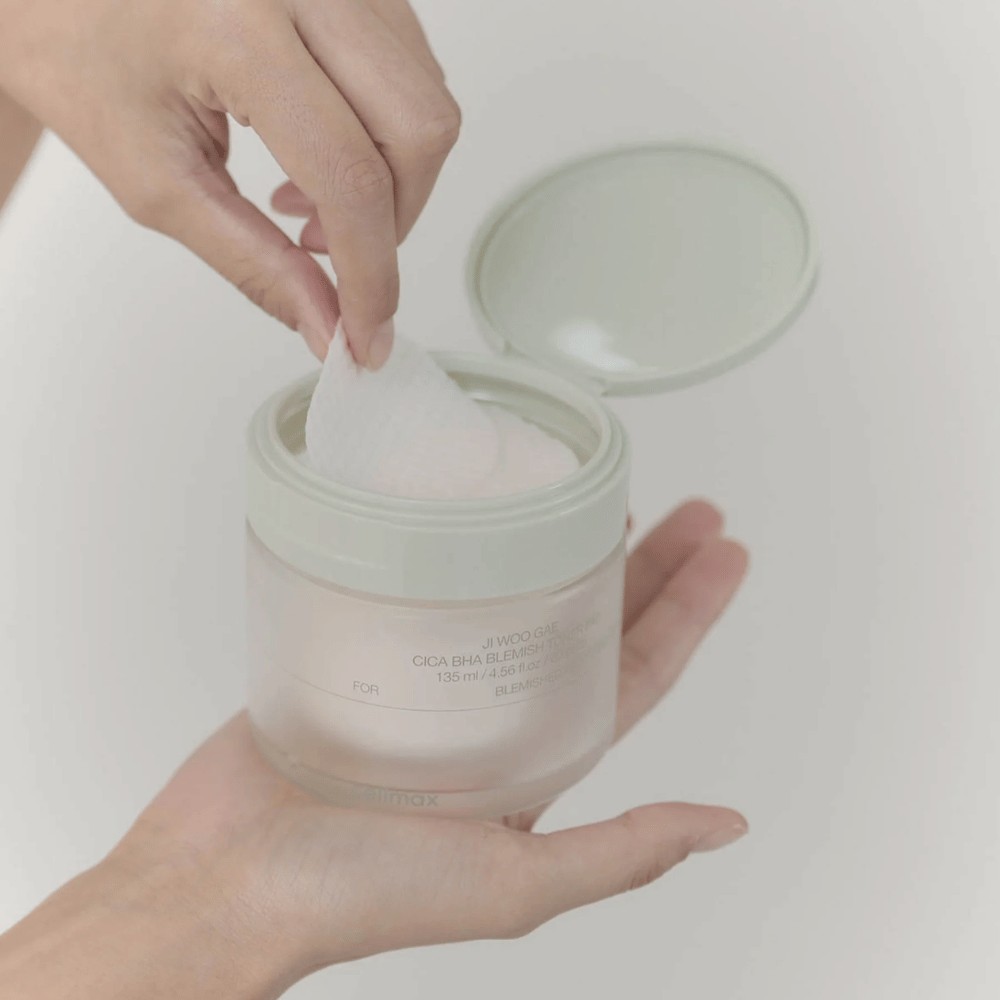 Hand pakt een toner pad uit de pot Celimax Ji Woo Gae Cica BHA Blemish Toner Pad, perfect voor onzuivere huid.