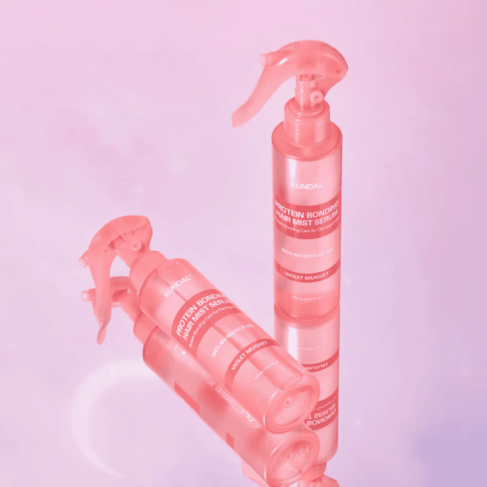 KUNDAL Protein Bonding Hair Mist Serum Violet Muguet in roze spuitflessen, staand en liggend tegen een lichtroze achtergrond met reflectie.