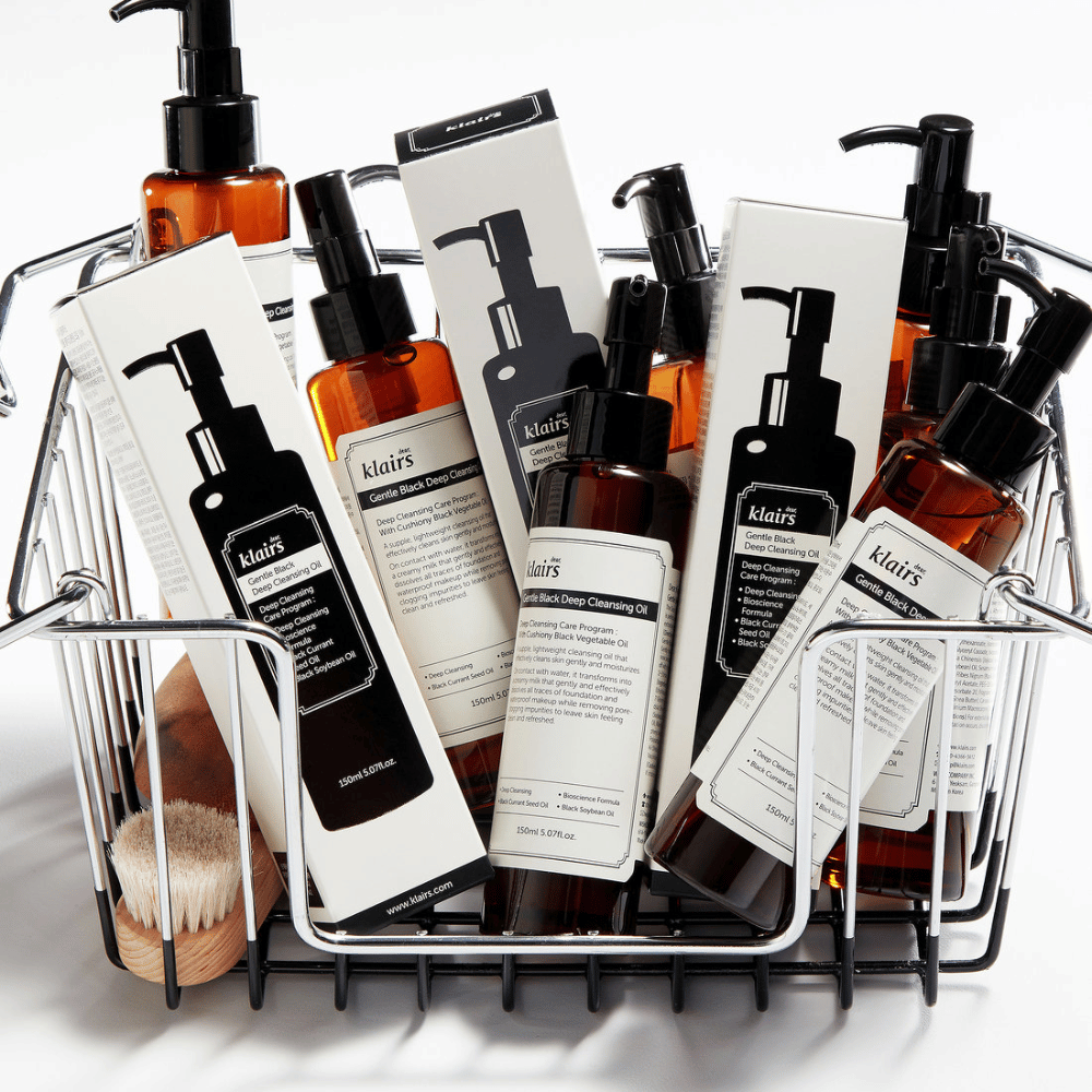 Een minishopwagen gevuld met huidverzorgingsproducten van Klairs, inclusief Gentle Black Deep Cleansing Oil in doorzichtige flessen met zwarte pompen en bijpassende verpakkingen.