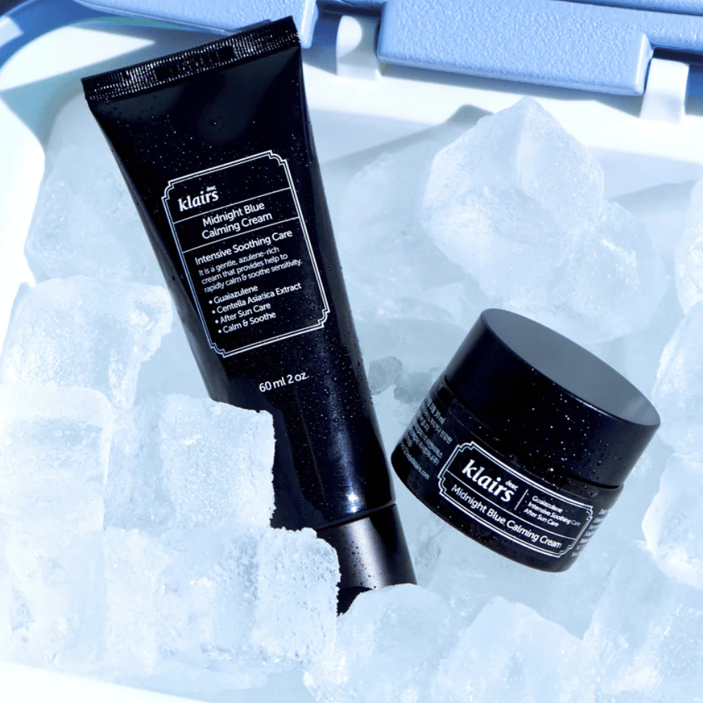 Een tube en pot van Klairs Midnight Blue Calming Cream liggen op ijsblokjes, met de nadruk op rustgevende en hydraterende eigenschappen, tegen een blauwe achtergrond.