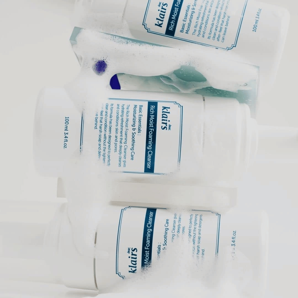 Drie flessen van Klairs Rich Moist Foaming Cleanser bedekt met schuim en waterdruppels, geplaatst op een wit oppervlak.