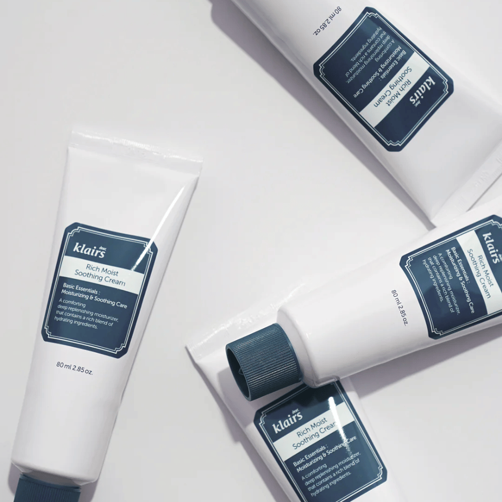 Meerdere tubes van Klairs Rich Moist Soothing Cream strategisch geplaatst op een lichte ondergrond, met schaduwen die diepte creëren.