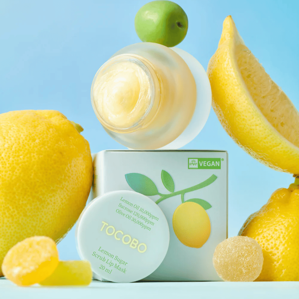 Pot met Tocobo Lemon Sugar Scrub Lip Mask geplaatst tussen citroenen en verpakking, gemarkeerd als veganistisch vriendelijk.