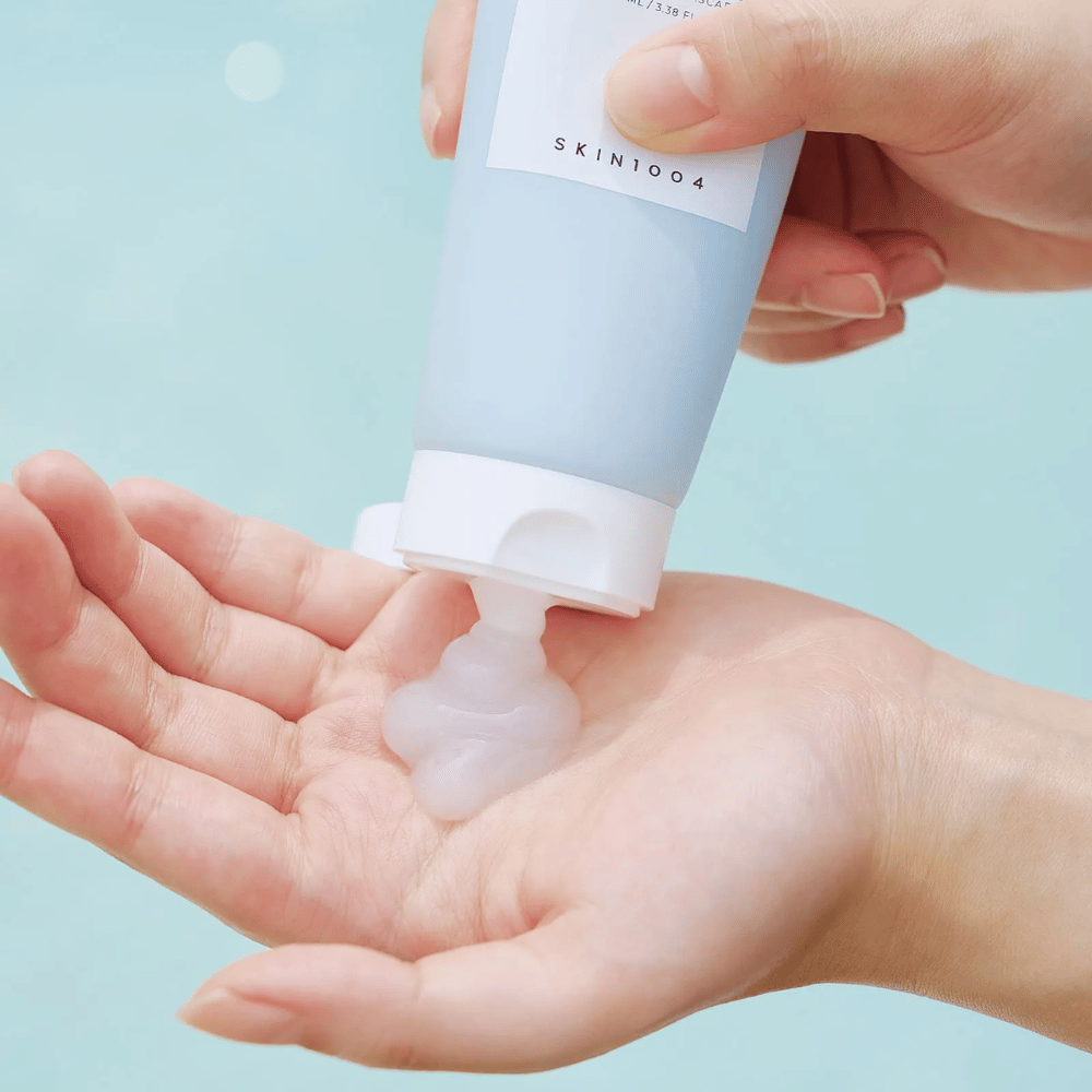 De afbeelding toont iemand die een heldere, gelachtige substantie uit een tube knijpt met het label "SKIN1004 Madagascar Centella Hyalu-Cica Sleeping Pack" dat 100 ml product bevat.