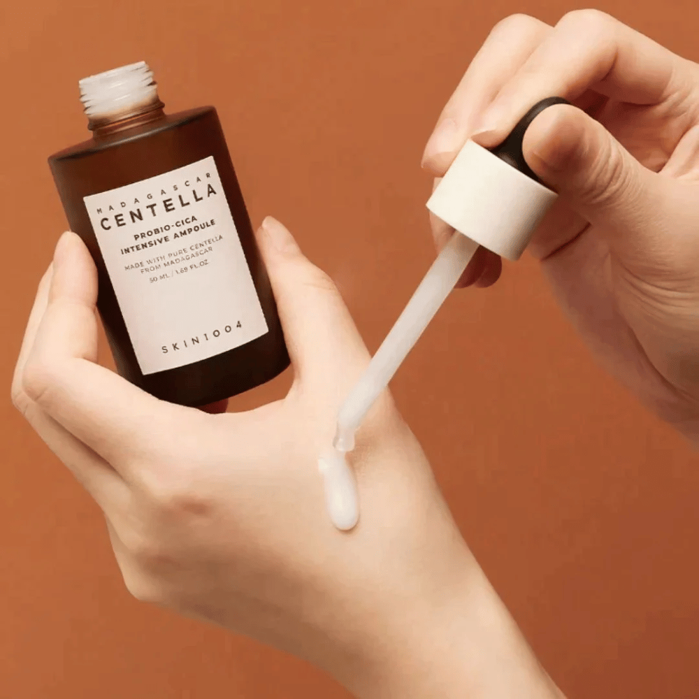 Handen die een druppelpipet gebruiken om "Madagascar Centella Probio-Cica Intensive Ampoule" van SKIN1004 te doseren.