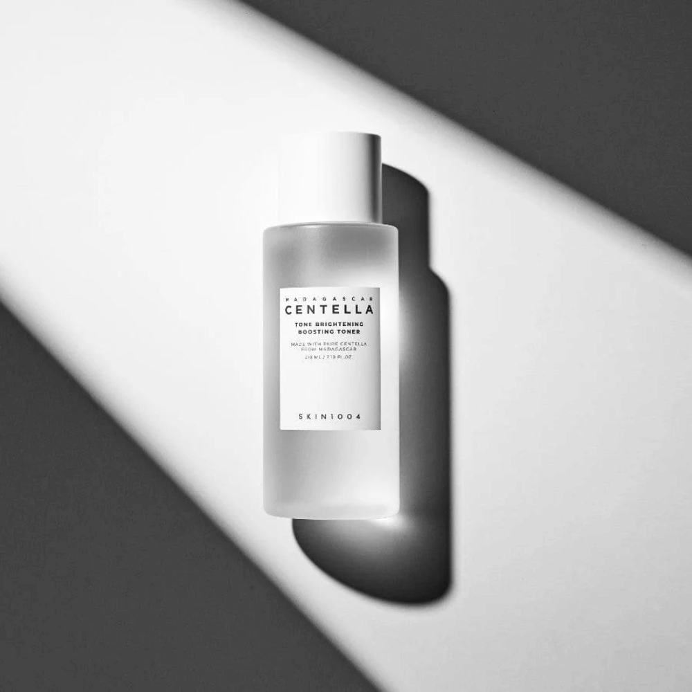 Fles van SKIN1004 Madagascar Centella Tone Brightening Boosting Toner liggend op een witte ondergrond met dramatische schaduw in zwart-wit lichtspel.