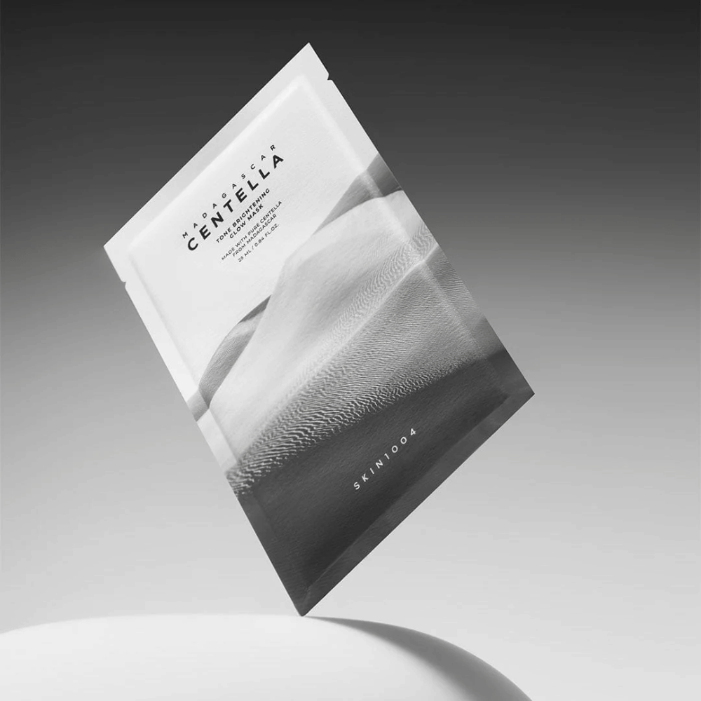 Sheet mask-verpakking van SKIN1004 zwevend tegen een grijze achtergrond met minimalistisch ontwerp.