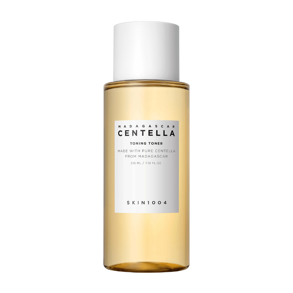 De afbeelding toont een fles met huidverzorgingstoner, gemerkt "Madagascar Centella Toning Toner" van SKIN1004. Het product wordt aangegeven 210 ml of 7.10 fl.oz te bevatten en is vervaardigd met pure Centella uit Madagaskar. De verpakking is eenvoudig en stijlvol met een doorzichtige fles en een gouden toner vloeistof erin, wat een gevoel van luxe en zuiverheid geeft. Het logo van het merk SKIN1004 is duidelijk zichtbaar aan de onderkant van het etiket.