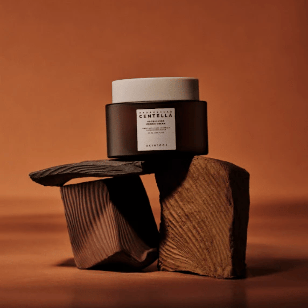 SKIN1004 Madagascar Centella Probio-Cica Enrich Cream in elegante bruine glazen pot op decoratieve houten blokken – voedende Koreaanse gezichtscrème die de huidbarrière versterkt.