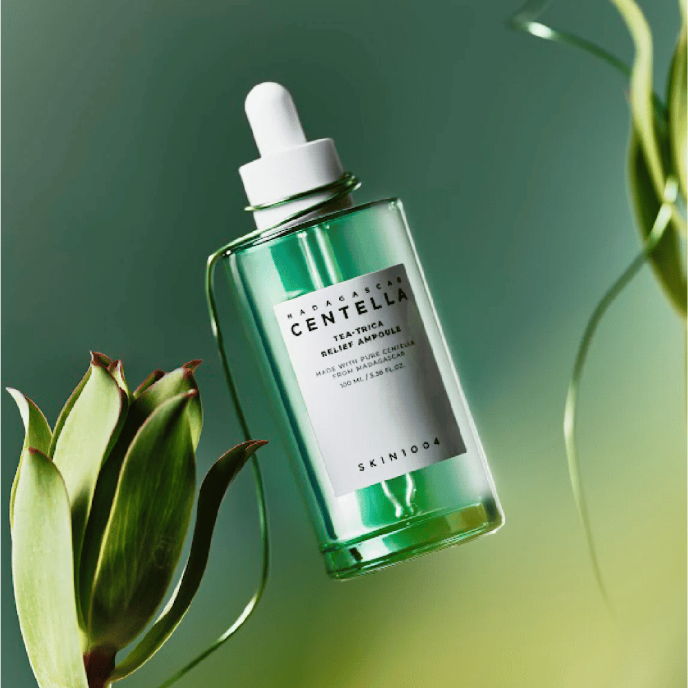 SKIN1004 Madagascar Centella Tea-Trica Relief Ampoule – groene glazen fles met pipet, wit etiket en 100 ml inhoud, gefotografeerd tegen groene achtergrond met plantendetails.