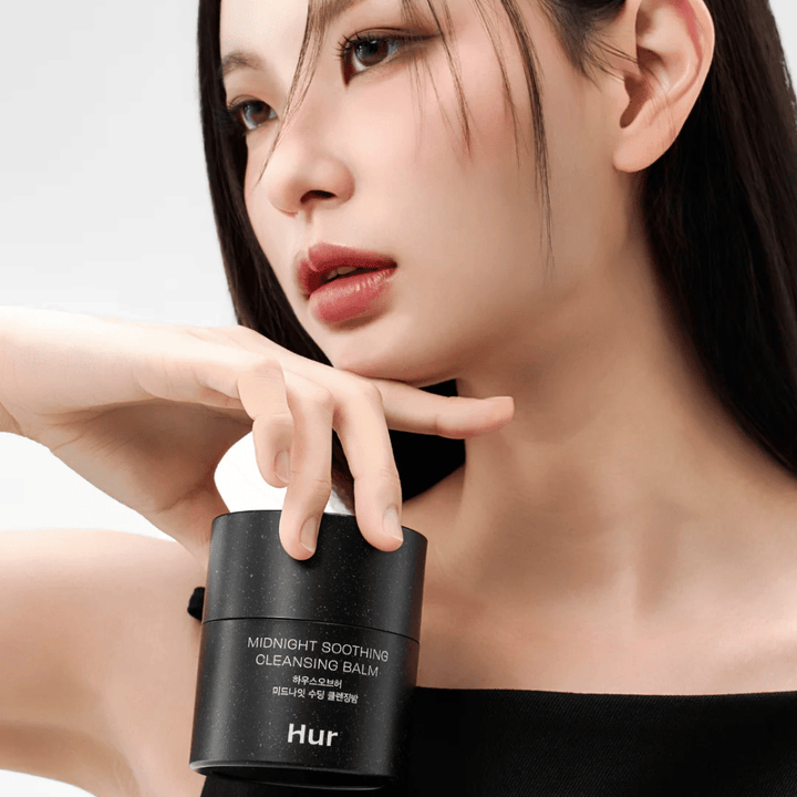 Model houdt Hoe Midnight Soothing Cleansing Balm vast. Koreaanse reinigingsbalsem die make-up effectief verwijdert en de huid reinigt zonder irritatie.