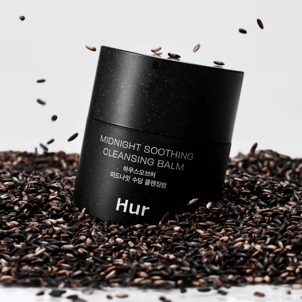 Hoe Midnight Soothing Cleansing Balm in zwarte pot geplaatst op zwarte zaden. Kalmerende reinigingsbalsem die make-up en onzuiverheden oplost terwijl de huid wordt verzorgd.