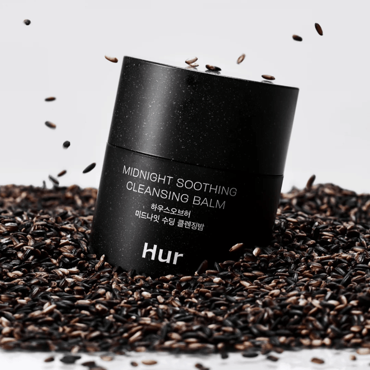 Hoe Midnight Soothing Cleansing Balm in zwarte pot geplaatst op zwarte zaden. Kalmerende reinigingsbalsem die make-up en onzuiverheden oplost terwijl de huid wordt verzorgd.