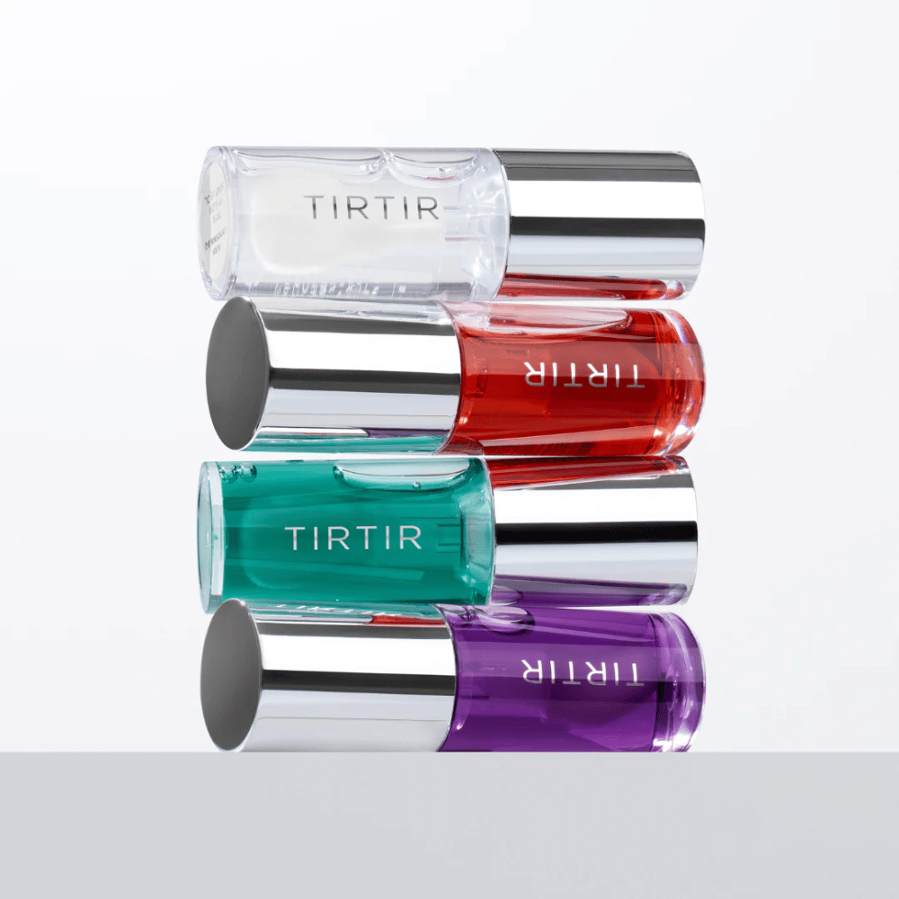 Vier TIRTIR My Glow Lip Oil in verschillende kleuren - transparant, rood, groen en paars - gestapeld op elkaar met zilverkleurige doppen tegen een witte achtergrond.