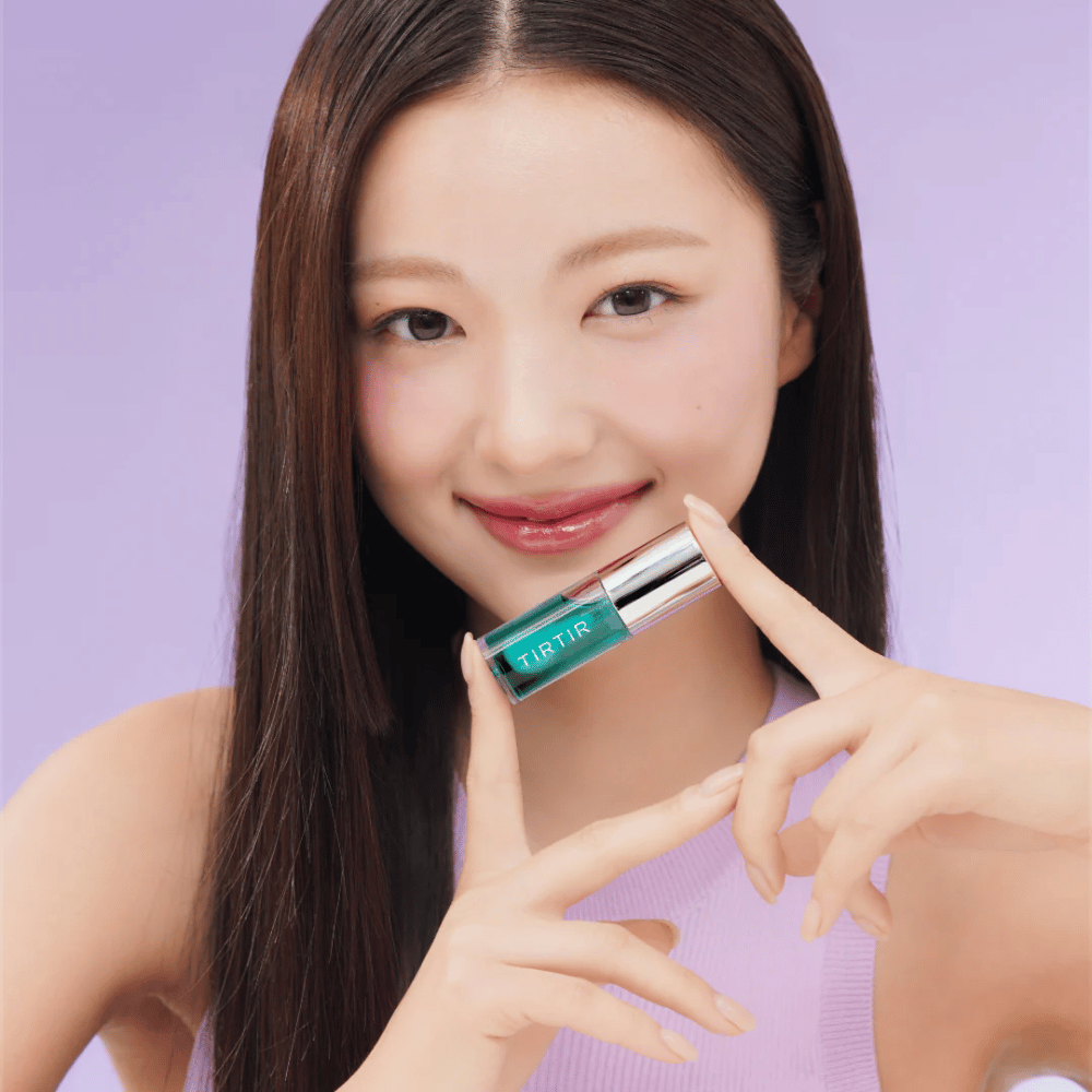 Vrouw met lang, steil haar houdt een TIRTIR My Glow Lip Oil vast en toont haar glanzende, roze lippen tegen een paarse achtergrond.