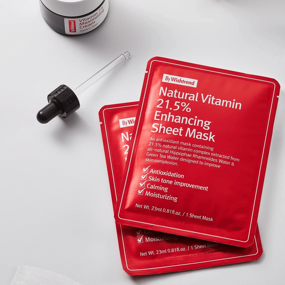 By Wishtrend Natural Vitamin 21.5% Enhancing Sheet mask in rode verpakkingen, geplaatst op een wit oppervlak samen met een pipet en een pot gezichtscrème.