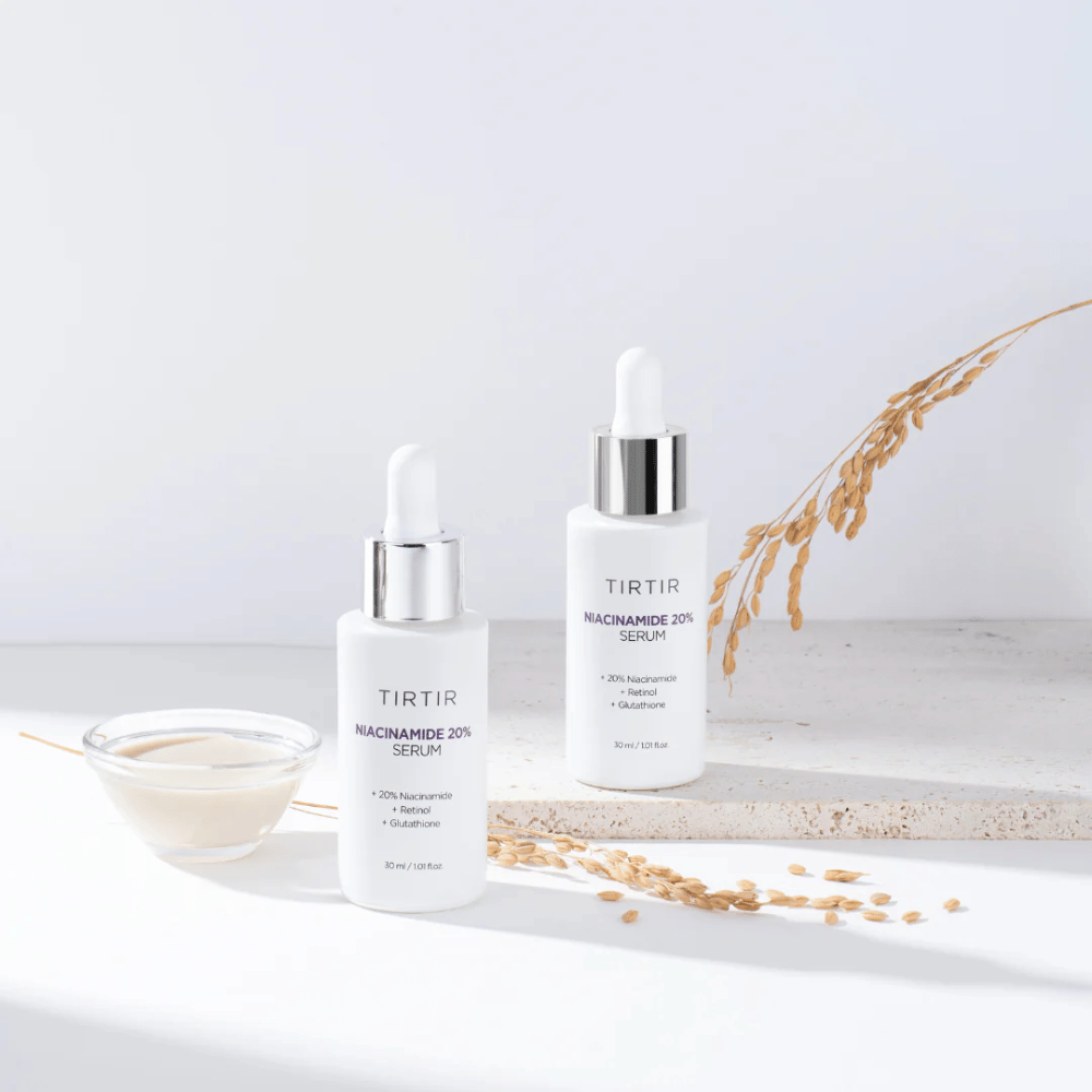 Twee flessen van Tirtirs "Niacinamide 20% Serum" worden getoond op een lichte ondergrond samen met een klein schaaltje met een romige substantie en enkele droge plantenstengels. Het serum bevat 20% niacinamide, retinol en glutathion, wat bijdraagt aan het verbeteren van het uiterlijk en de textuur van de huid.