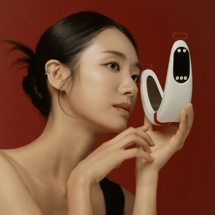 Model houdt Beaund Nmode Pro voor het gezicht tegen een rode achtergrond. De afbeelding benadrukt het elegante ontwerp van het apparaat, het digitale display en het compacte formaat.