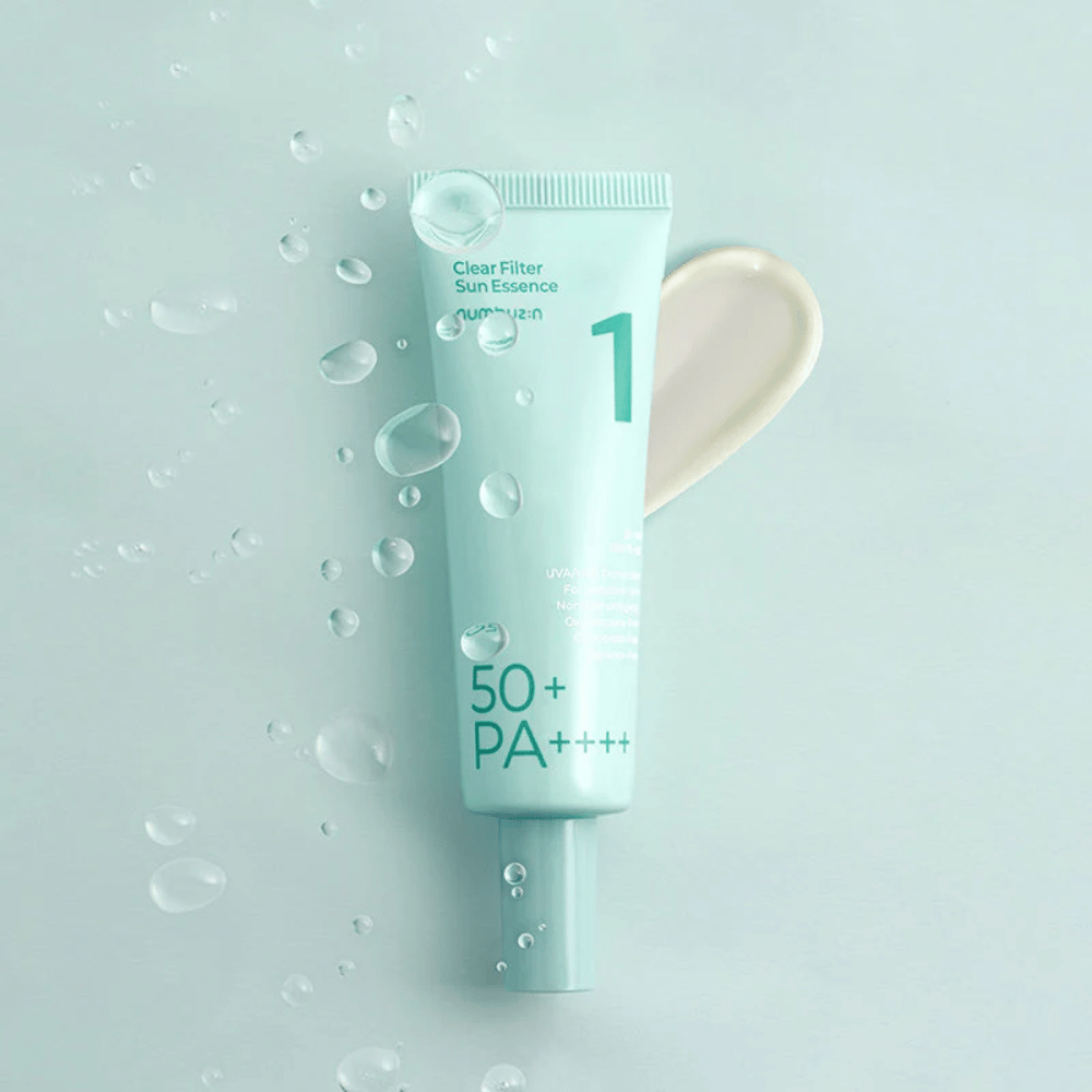 Een lichtblauwe tube met No.1 Clear Filter Sun Essence SPF 50+ PA++++. De tube is versierd met waterdruppels en een beetje van het product wordt ernaast getoond. Het product is ontworpen om een hoge zonnebeschermingsfactor en bescherming tegen UVA/UVB-stralen te bieden.